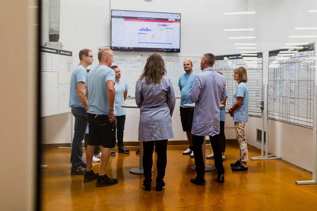 Skupina sodelavcev v proizvodnji stoji v krogu in imajo sestanek.