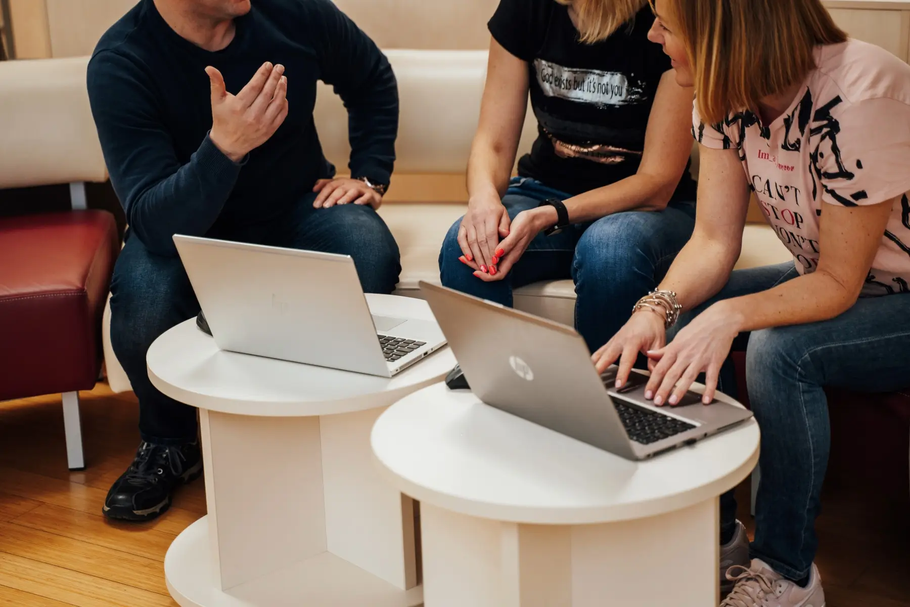 Skupina treh oseb sedi okoli majhnih miz, uporablja prenosne računalnike in razpravlja o HR temah. Ena oseba gestikulira, medtem ko druga tipka na računalnik.